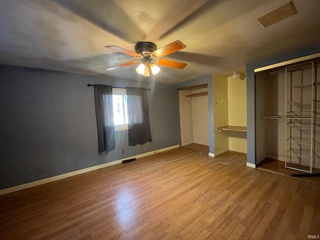 unfurnished bedroom featuring baseboards, wood finished floors, visible vents, and multiple closets