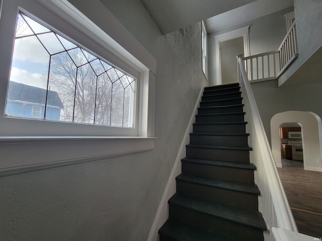 staircase with a healthy amount of sunlight, baseboards, arched walkways, and wood finished floors