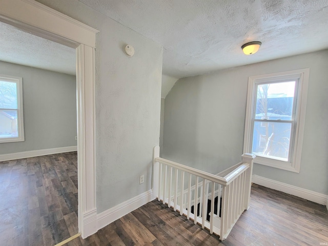 stairs with a healthy amount of sunlight, a textured ceiling, baseboards, and wood finished floors