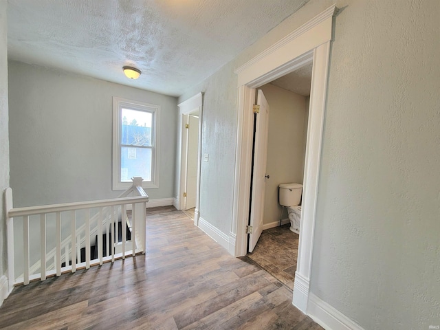 corridor featuring a textured wall, a textured ceiling, an upstairs landing, and wood finished floors