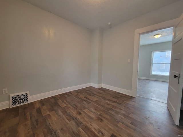 unfurnished room with dark wood-type flooring, visible vents, a textured ceiling, and baseboards