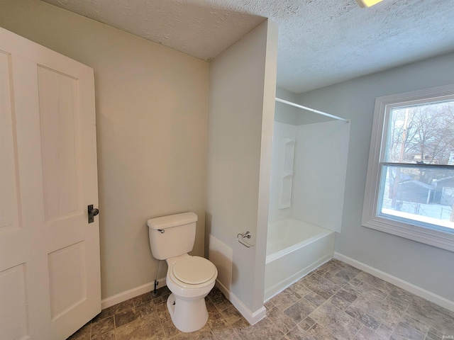 bathroom with baseboards, bathing tub / shower combination, toilet, stone finish flooring, and a textured ceiling