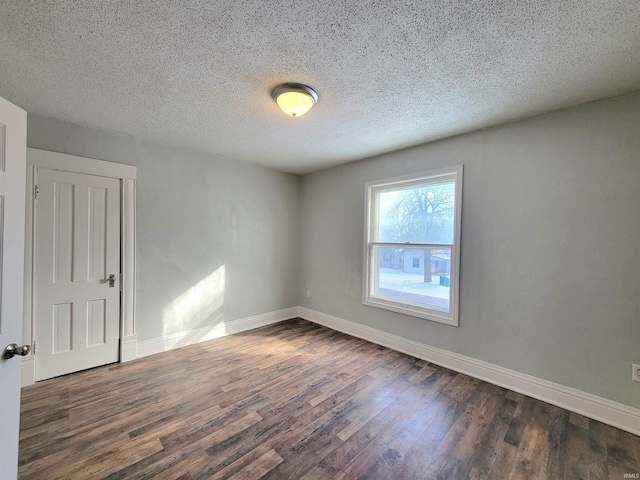 empty room with a textured ceiling, baseboards, and dark wood-type flooring