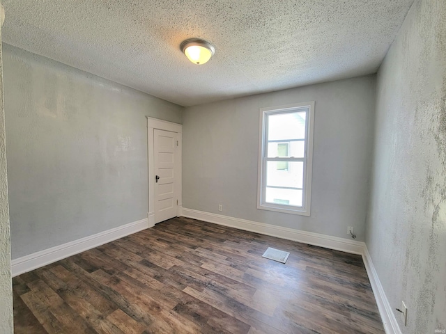 unfurnished room featuring dark wood-style floors, a textured wall, a textured ceiling, and baseboards