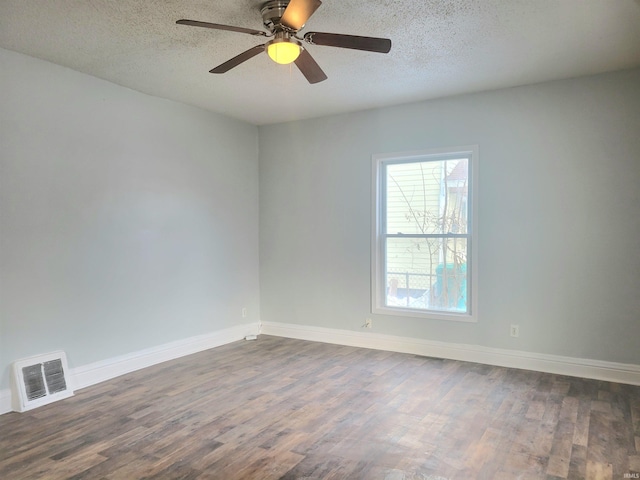 empty room featuring dark wood-style floors, visible vents, a textured ceiling, and baseboards