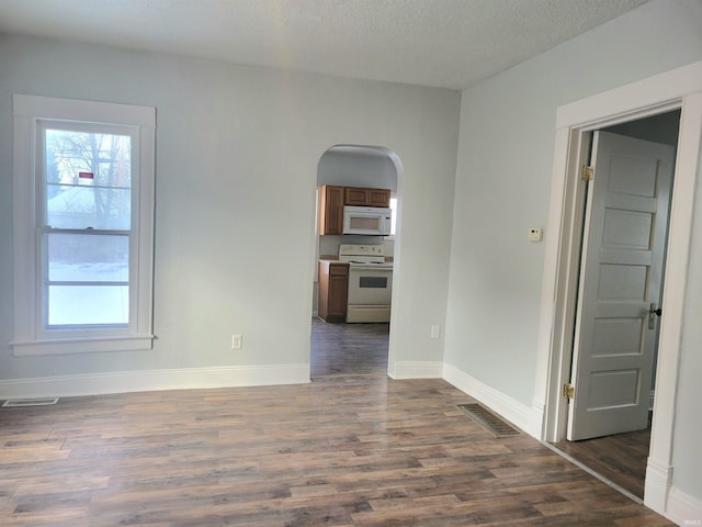 empty room with arched walkways, visible vents, dark wood-style floors, and a wealth of natural light