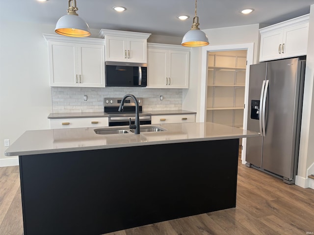 kitchen with appliances with stainless steel finishes, pendant lighting, a sink, and wood finished floors