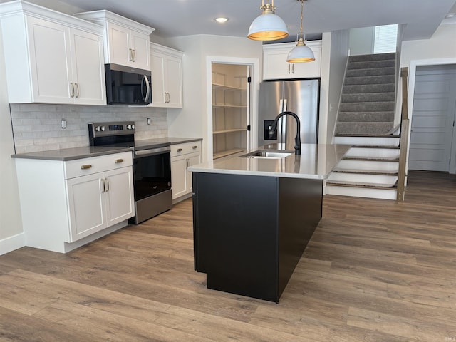 kitchen featuring backsplash, appliances with stainless steel finishes, white cabinets, a sink, and wood finished floors