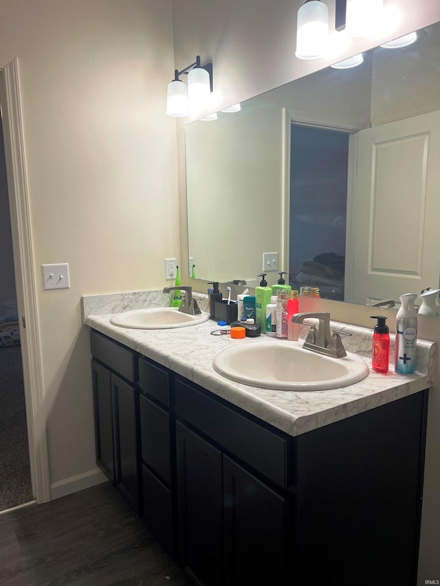 full bath featuring double vanity, baseboards, a sink, and wood finished floors