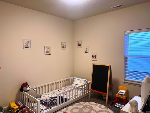 carpeted bedroom featuring a nursery area and visible vents