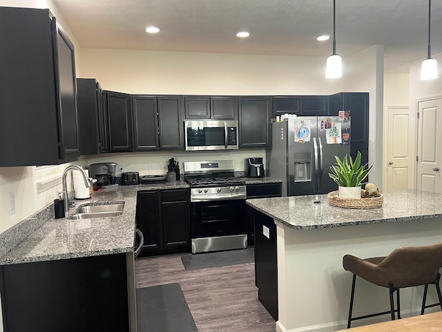 kitchen with a breakfast bar area, stainless steel appliances, dark wood-type flooring, a sink, and light stone countertops