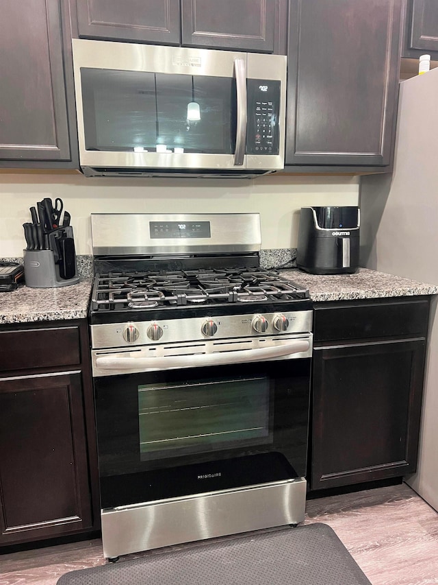 kitchen with stainless steel appliances, dark brown cabinets, light wood-style flooring, and light stone counters