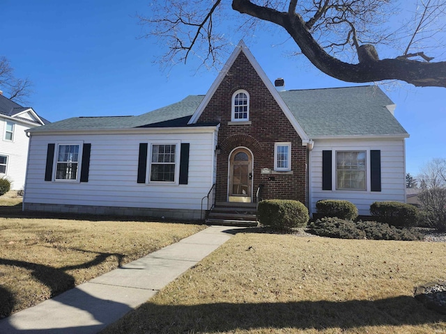 view of front of home with a shingled roof, a front yard, and brick siding