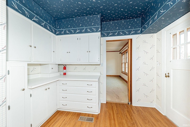 kitchen featuring light countertops, visible vents, white cabinets, light wood-type flooring, and baseboards