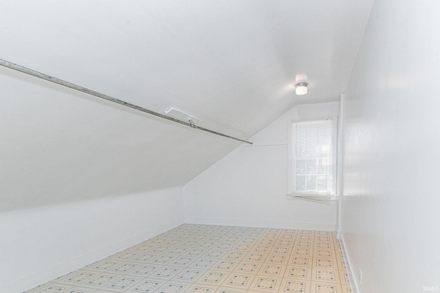 additional living space with baseboards, vaulted ceiling, and light floors