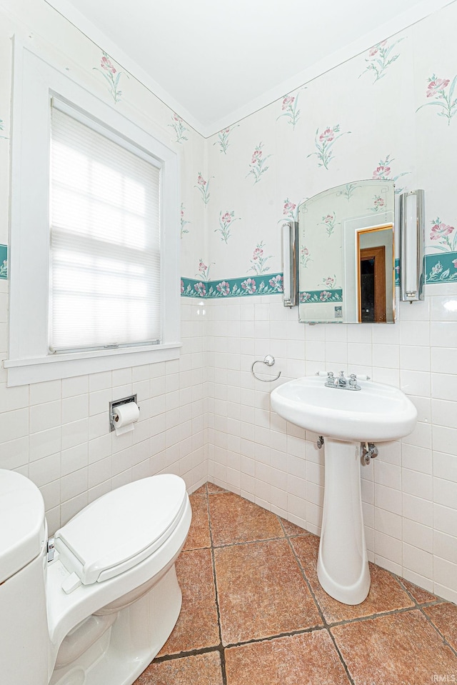 bathroom with a wainscoted wall, a sink, toilet, and wallpapered walls