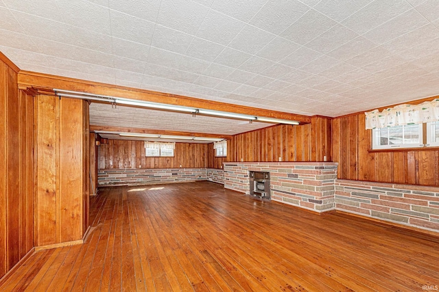 unfurnished living room featuring wood-type flooring, wood walls, a wood stove, and brick wall