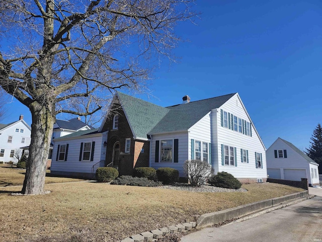 view of front of house with an outbuilding, brick siding, roof with shingles, a front lawn, and a chimney