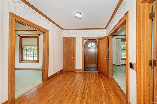 foyer entrance with ornamental molding, wood finished floors, baseboards, and wallpapered walls