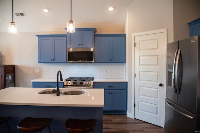 kitchen featuring blue cabinetry, decorative backsplash, appliances with stainless steel finishes, a sink, and a kitchen bar