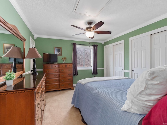 bedroom with light carpet, attic access, ornamental molding, a textured ceiling, and two closets