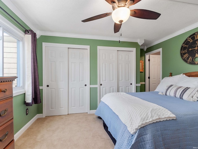 bedroom with light carpet, baseboards, ornamental molding, a textured ceiling, and two closets