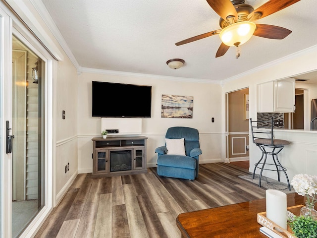 living area featuring crown molding, a textured ceiling, baseboards, and wood finished floors