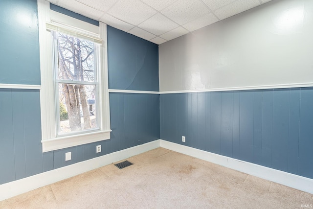 carpeted empty room with a drop ceiling, visible vents, and a healthy amount of sunlight