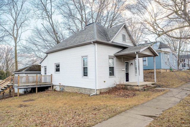 view of front facade with a shingled roof, a deck, and a front yard