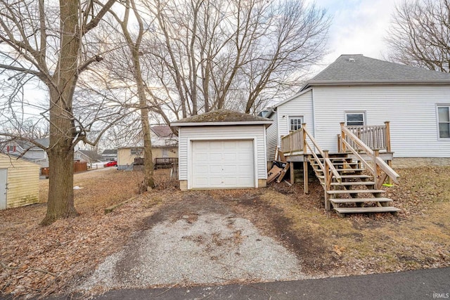 exterior space with an outdoor structure, a detached garage, driveway, stairway, and roof with shingles