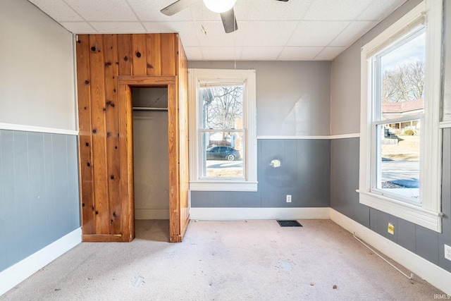 unfurnished bedroom with a paneled ceiling, multiple windows, carpet, and visible vents