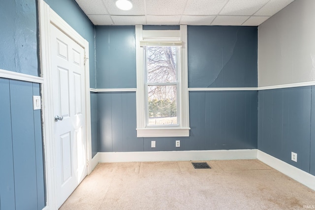 spare room with a paneled ceiling, carpet, visible vents, and baseboards