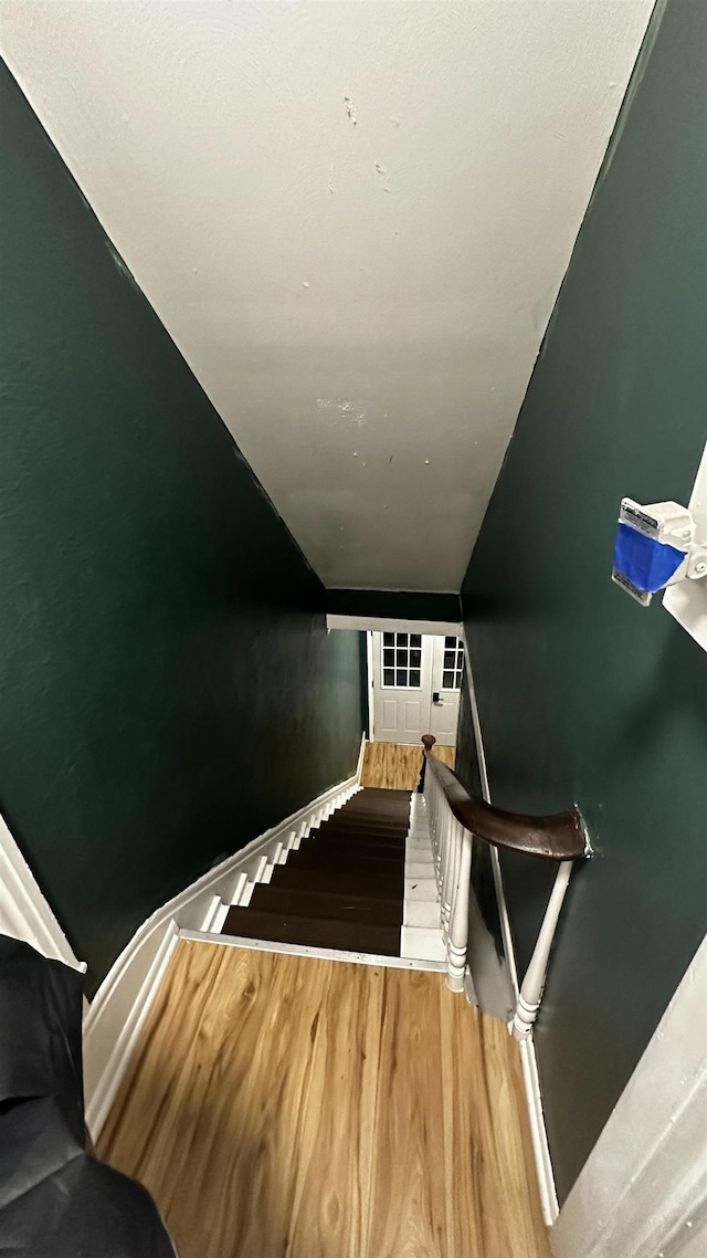 staircase featuring lofted ceiling, baseboards, and wood finished floors