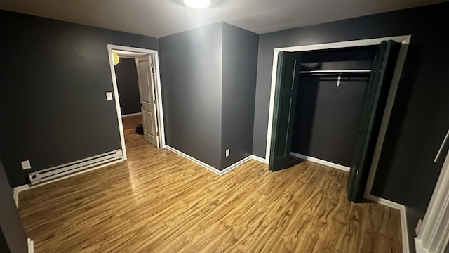 unfurnished bedroom with a closet, baseboards, baseboard heating, and wood finished floors