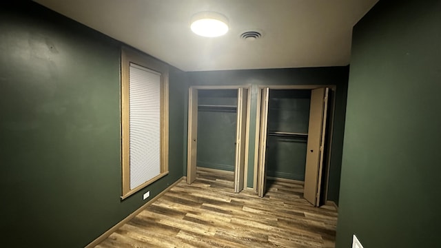 corridor with baseboards, visible vents, and wood finished floors