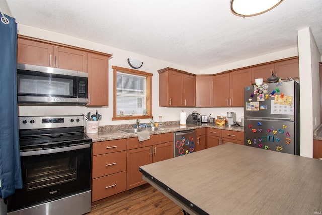 kitchen with dark wood-style flooring, stainless steel appliances, brown cabinetry, a sink, and a textured ceiling