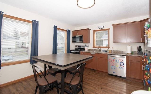 kitchen with dark wood-style flooring, appliances with stainless steel finishes, stone countertops, a sink, and baseboards