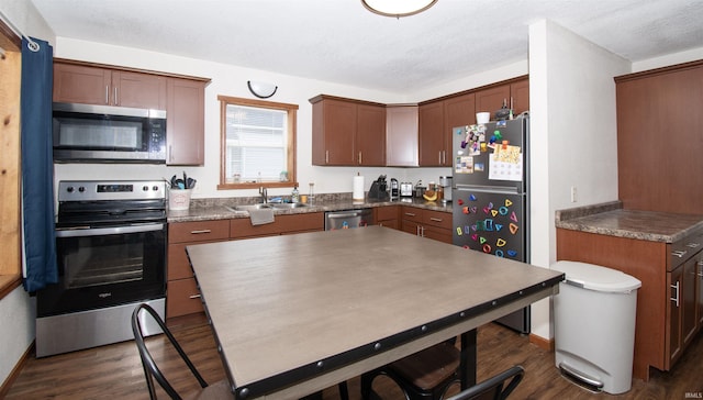 kitchen with dark countertops, dark wood-style flooring, stainless steel appliances, and a sink