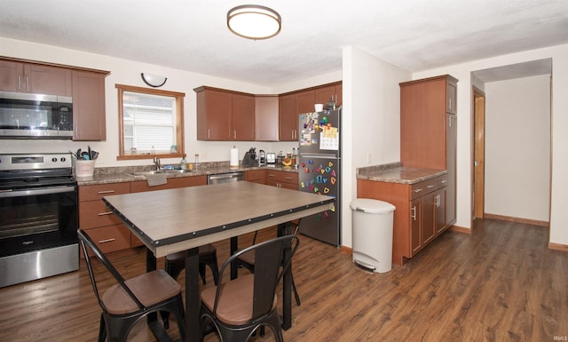 kitchen with appliances with stainless steel finishes, dark wood-type flooring, a sink, and baseboards