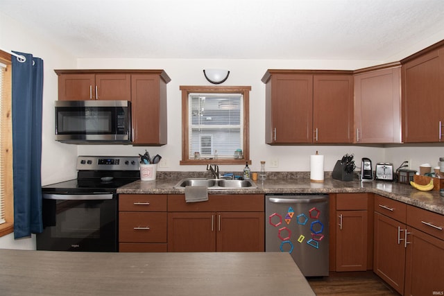 kitchen featuring stainless steel appliances, dark wood-type flooring, dark countertops, and a sink