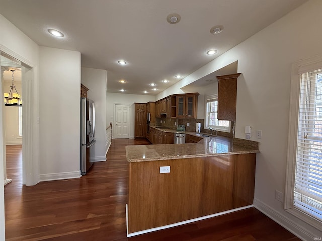 kitchen featuring glass insert cabinets, dark wood-type flooring, a peninsula, stainless steel appliances, and a sink