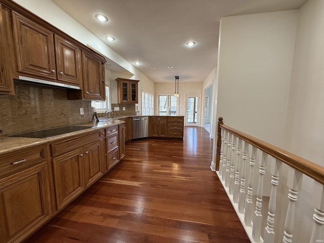 kitchen with black electric stovetop, under cabinet range hood, dark wood-style flooring, stainless steel dishwasher, and glass insert cabinets