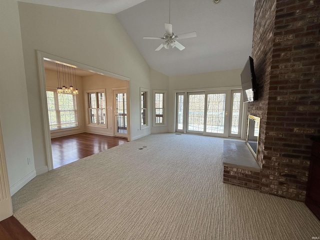 unfurnished living room with high vaulted ceiling, ceiling fan with notable chandelier, carpet floors, baseboards, and a brick fireplace