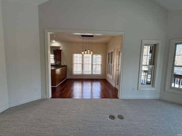 empty room featuring dark colored carpet, lofted ceiling, and baseboards