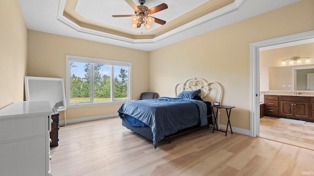 bedroom with connected bathroom, a ceiling fan, baseboards, light wood-type flooring, and a tray ceiling