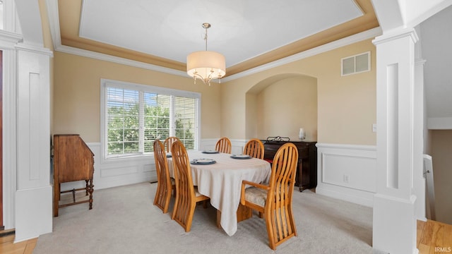 dining area featuring visible vents, light colored carpet, a wainscoted wall, a tray ceiling, and ornate columns