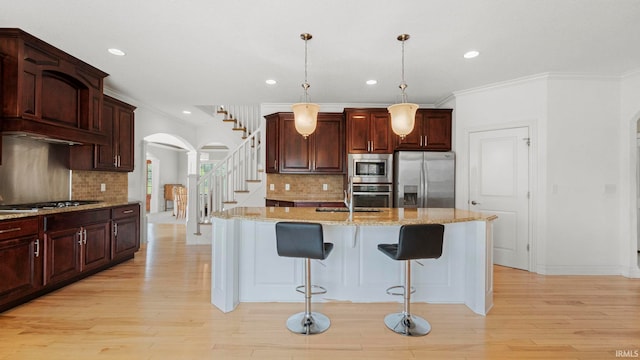 kitchen featuring light stone counters, arched walkways, stainless steel appliances, light wood-style floors, and a kitchen breakfast bar