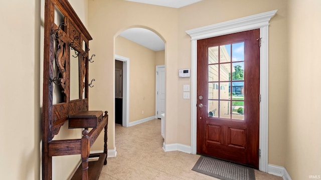 doorway to outside featuring arched walkways, light tile patterned flooring, and baseboards