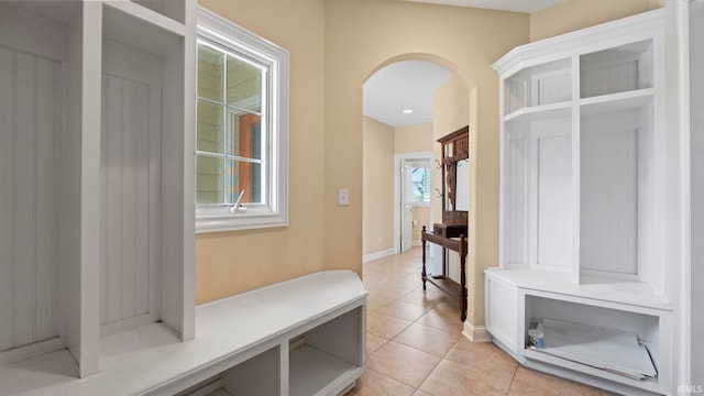 mudroom with arched walkways, light tile patterned flooring, and baseboards