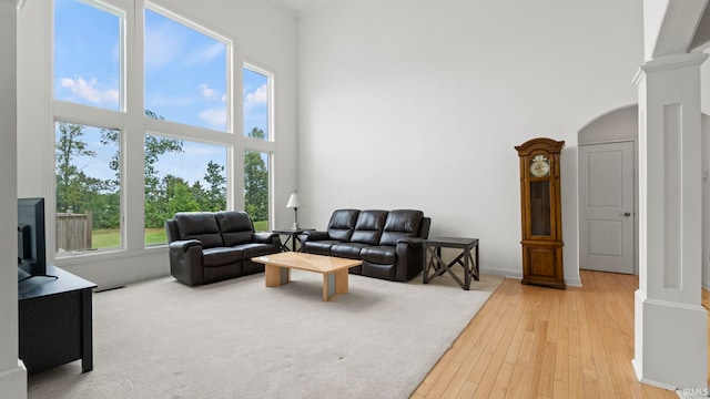 living area with a towering ceiling, ornate columns, arched walkways, and light wood finished floors